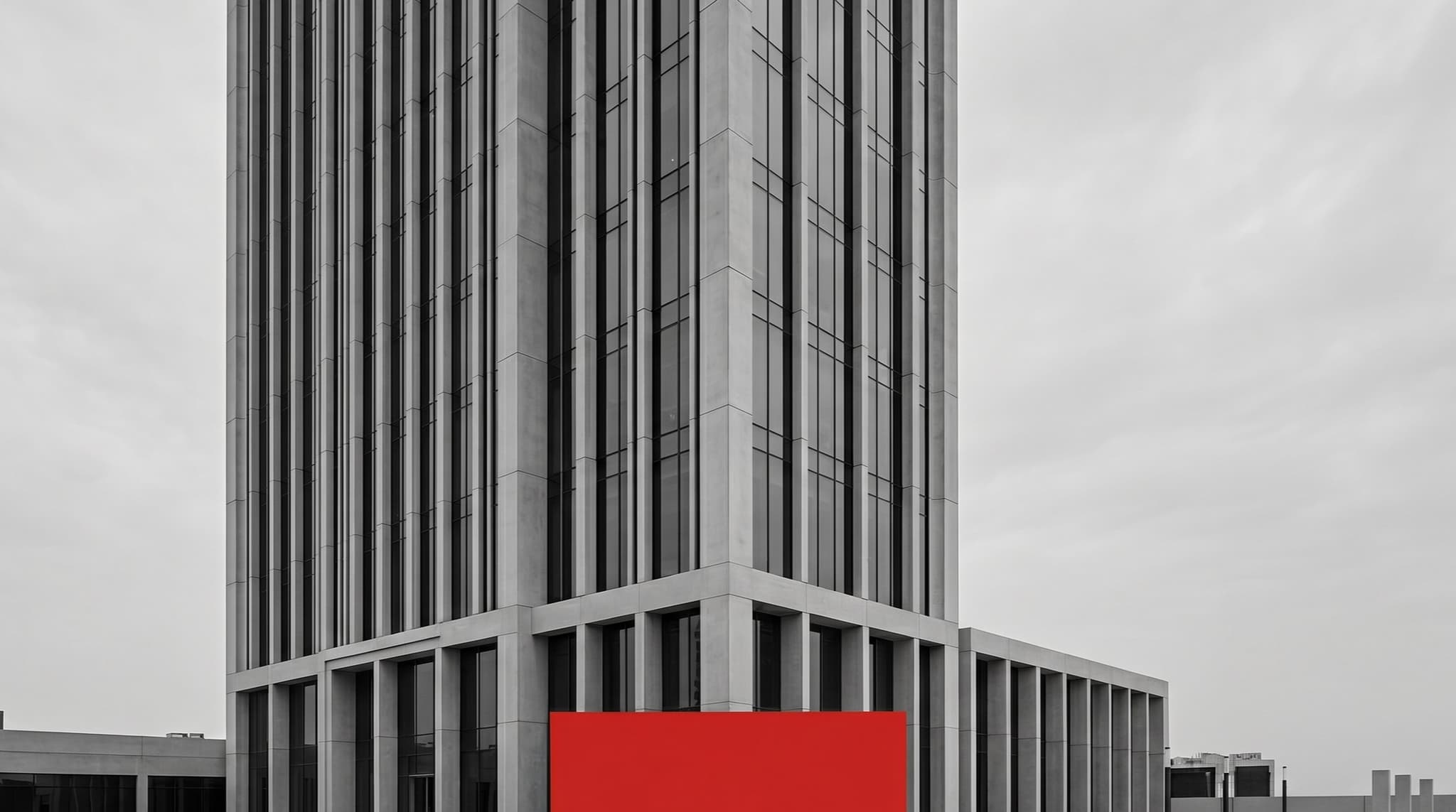 A modern Dubai office tower exterior with geometric concrete and glass facade, a single red banner panel as the only colour accent in the plaza below